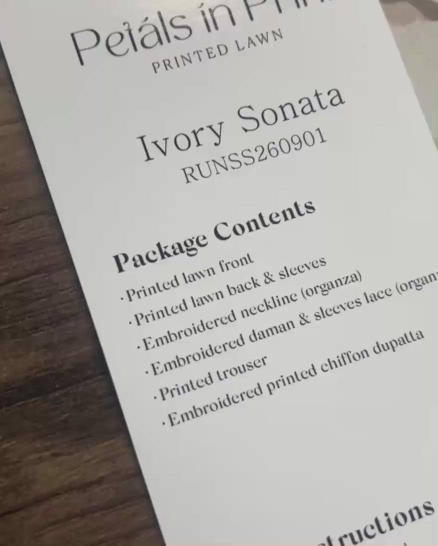 Product label for Roheenaz Ivory Sonata from the Petals in Prints printed lawn collection, showing package contents and a folded plaid fabric swatch on a wooden surface